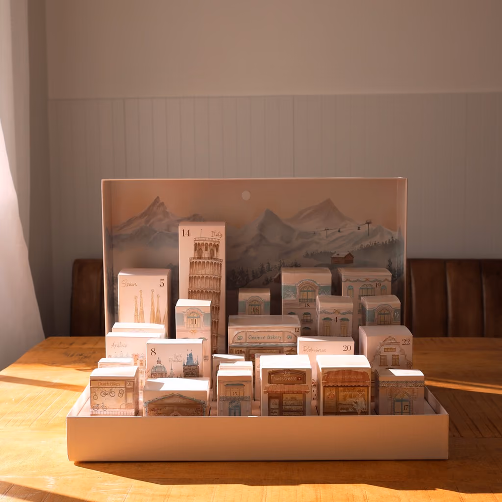 The open calendar on a wooden table, 24 closed boxes shaped as European buildings before a mountain backdrop