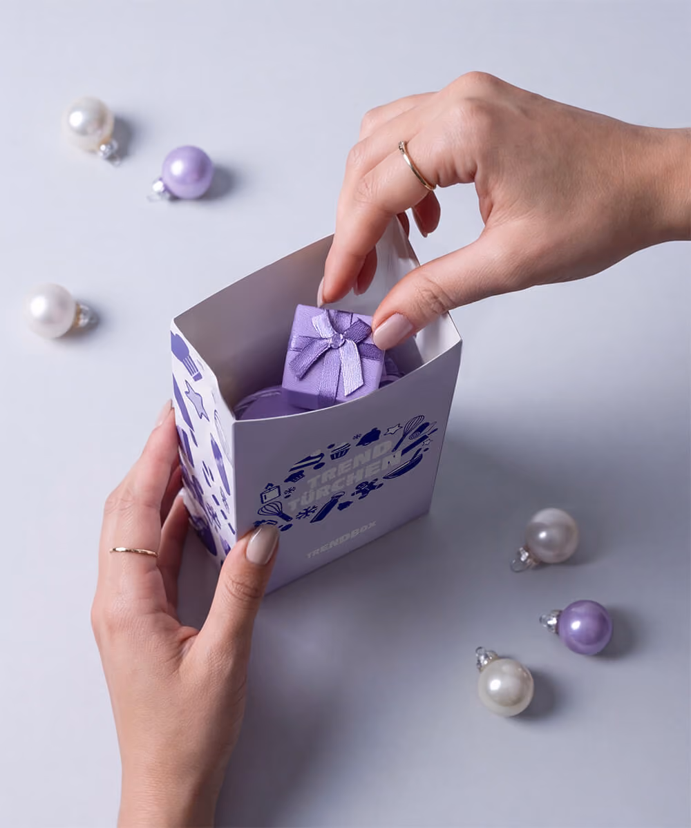 Hands lifting a small wrapped gift out of one lilac door carton