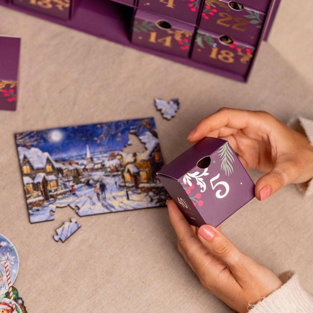 A finished wooden puzzle of a snowy village beside its numbered drawer box