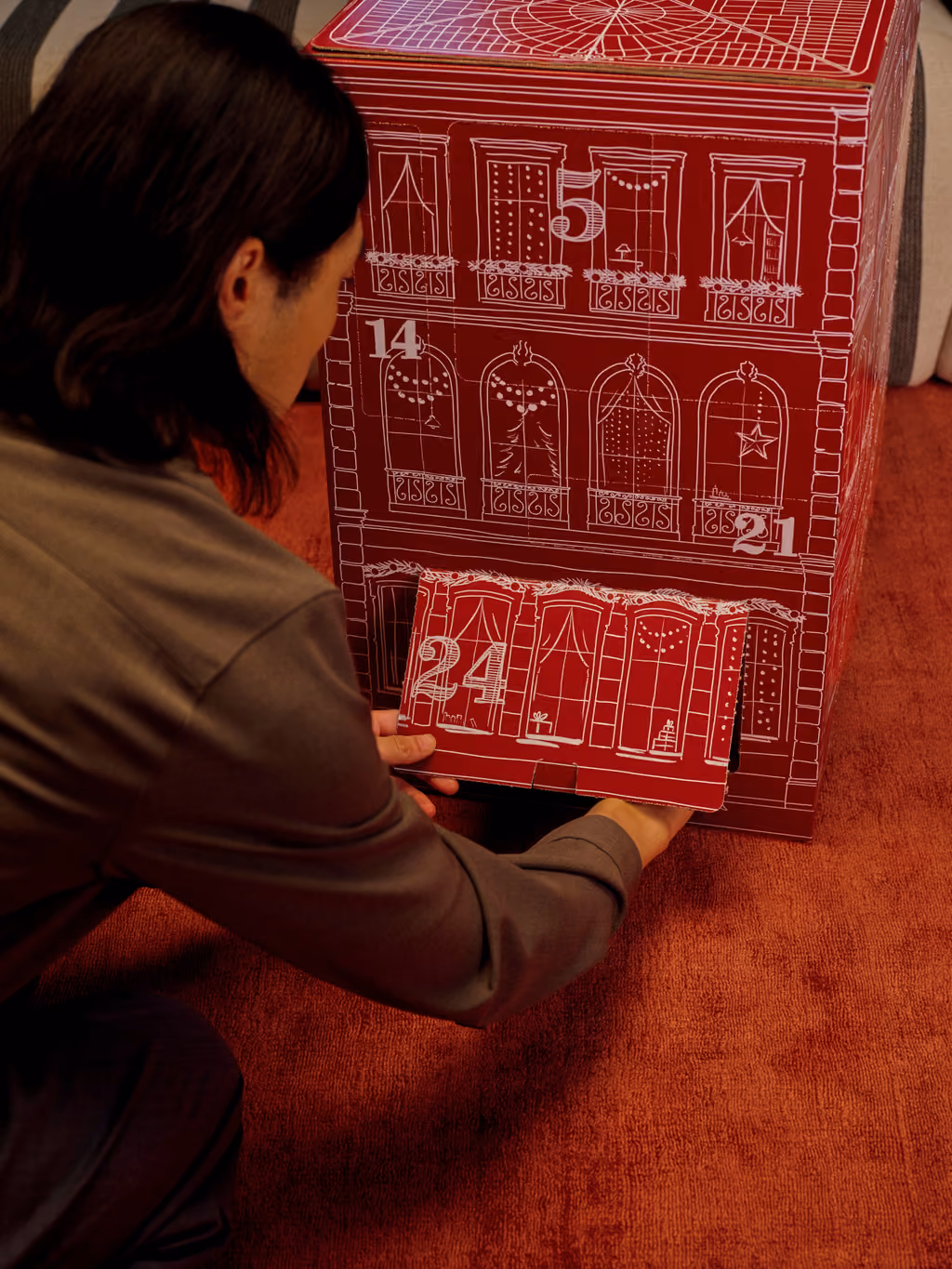 Someone kneeling on a red carpet pulling open the wide door numbered 24